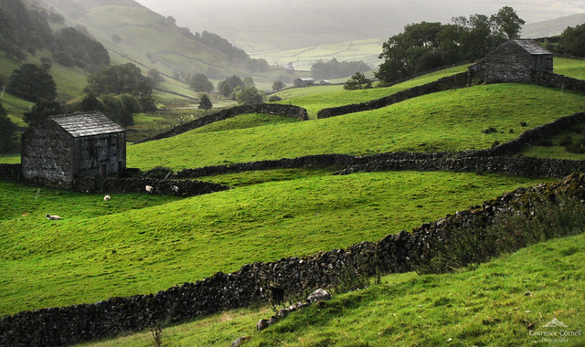 Two dark stone barns in a valley